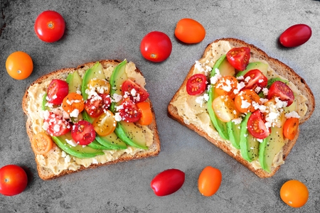 Avocado toasts with hummus and tomatoes, overhead view on rustic metallic backgroundの写真素材