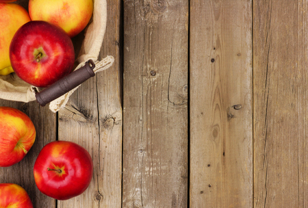 Freshly harvested apples with basket, side border on a rustic aged wood backgroundの写真素材