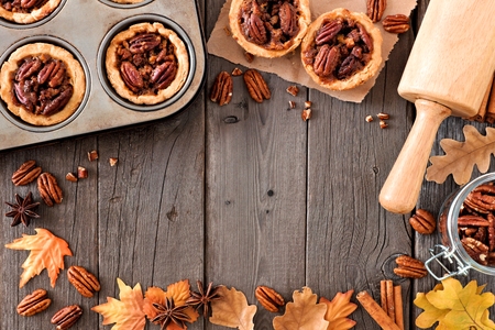 Autumn baking scene frame with pecan tarts, leaves and nuts over a wood backgroundの写真素材