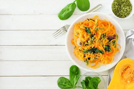 Butternut squash spirilized noodles with spinach and pumpkin seeds on white wood background, Healthy eating concept. Top view, side border.の写真素材