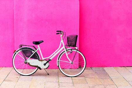 Vintage white bicycle with basket against a vibrant pink wallの写真素材