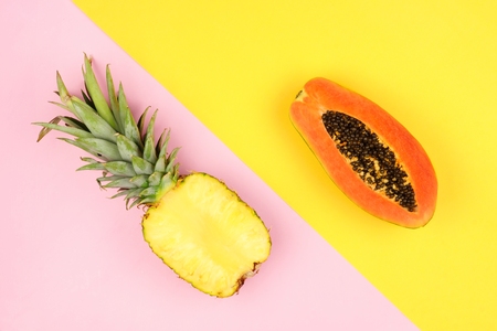 Half cut juicy pineapple and mango on a pastel pink and yellow background. Minimal summer concept. Angular orientation.の写真素材