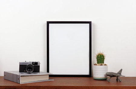 Mock up black frame with travel theme decor on a shelf or desk. Wood shelf and white wall. Portrait frame orientation.の写真素材