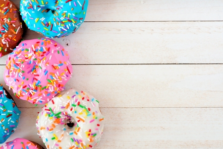 Side border of assorted donuts with pastel colored icing and sprinkles against a white wood backgroundの写真素材