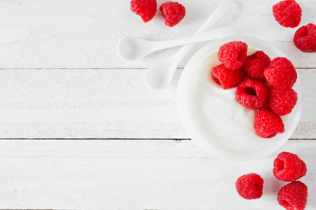 Healthy yogurt with raspberries. Overhead corner border on a white woodの写真素材
