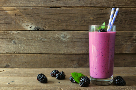 Healthy blackberry smoothie in a tall glass with scattered berries over a rustic woodの写真素材