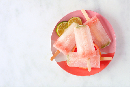 Sparkling lime and grapefruit ice lolly on a plate, top view against a marble backgroundの写真素材