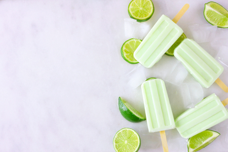 Lime yogurt ice lolly side border, top view against a marble background with copy spaceの写真素材