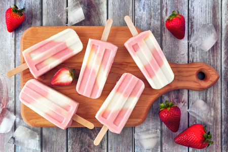 Healthy strawberry yogurt summer popsicles on a serving board, top view table scene against a rustic woodの写真素材