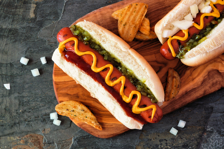 Hot dogs and potato wedges on wooden board, close up, top viewの写真素材