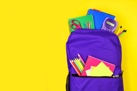 Purple backpack full of school supplies against a bright yellow background, top view with copy spaceの写真素材