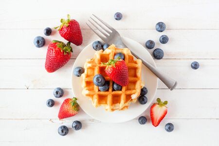 Breakfast waffles with scattered strawberries and blueberries, top view over a white wood backgroundの写真素材