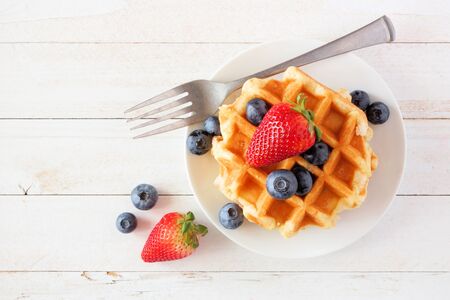 Breakfast waffles with strawberries and blueberries, top view over a white wood backgroundの写真素材