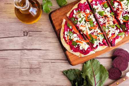 Beet hummus flat bread with feta cheese, top view corner border with copy space against a wood...