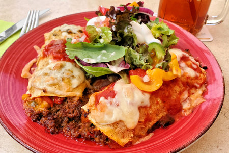 Mexican enchiladas with ground beef, peppers, cheese and salsa, close up on a red plateの写真素材