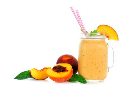 Peach smoothie in a mason jar glass with scattered fruit isolated on a white backgroundの写真素材