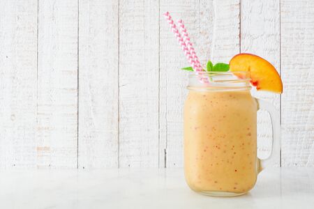 Peach smoothie in a mason jar glass, side view with a white wood backgroundの写真素材
