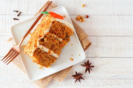 Slice of homemade carrot cake with cream cheese frosting, top view table scene over white woodの写真素材