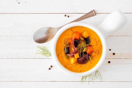 Roasted autumn vegetable soup in an onion soup bowl, top view on white woodの写真素材