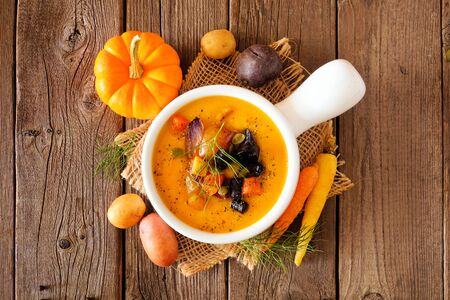Homemade roasted autumn vegetable soup in an onion soup bowl, above view table scene on rustic woodの写真素材