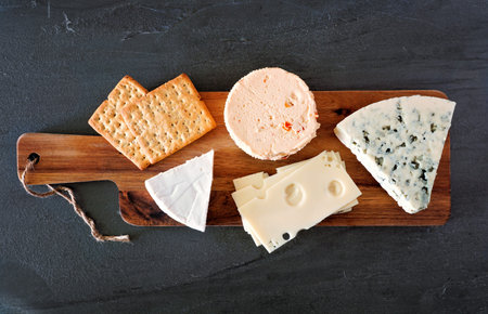 Cheese platter with a selection of cheeses on wooden serving board on a slate background