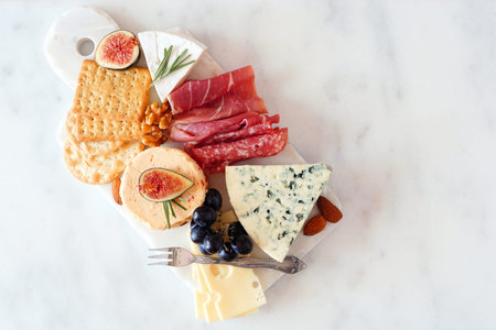 Appetizer platter with assorted cheeses and meats, top view on white marble