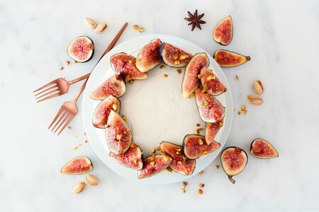 Fig spice cake with pistachios and white frosting, top view with frame of ingredients over white marbleの写真素材
