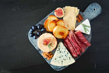 Appetizer platter with assorted cheeses and meats, overhead view on a dark stone backgroundの写真素材