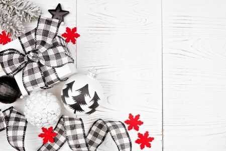 Christmas corner border of black and white checked buffalo plaid ribbon, gifts and ornaments, overhead on a white wood backgroundの写真素材