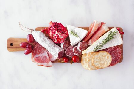 Serving board of assorted meats, cheeses and appetizers, top view on white marbleの写真素材