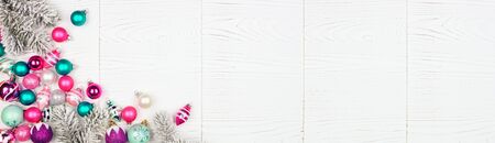 Christmas corner border banner with pink, purple and teal baubles and snowy branches, above view on a white wood backgroundの写真素材