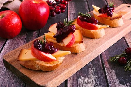 Holiday crostini appetizers with cranberries, apple and gouda cheese, close up table scene against dark woodの写真素材