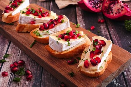 Holiday crostini appetizers with brie cheese, pomegranates and parsley, close up on a serving board against rustic woodの写真素材