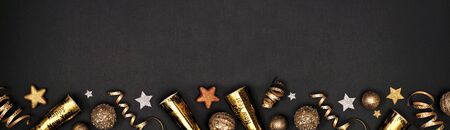 New Years Eve border banner of glittery gold stars, streamers, decorations and noisemakers, above view over a black backgroundの写真素材