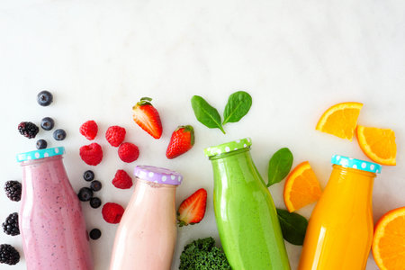 Assorted healthy fruit smoothies in bottles with ingredients, top view against white marble