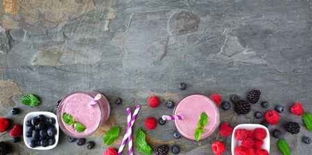 Banner with healthy mixed berry smoothie bottom border, top view over a dark stone backgroundの写真素材