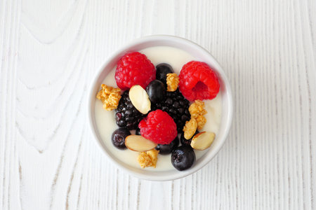 Bowl of yogurt with healthy fresh berries and granola. Close up top view on a white wood background.