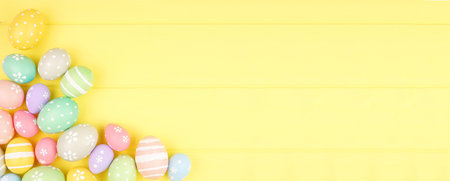 Easter banner with corner border of pastel Easter Eggs over a yellow wood background with copy space