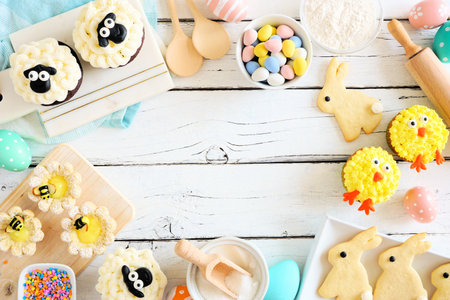 Easter or spring baking scene of various sweets and cookies, above view frame over a white wood...