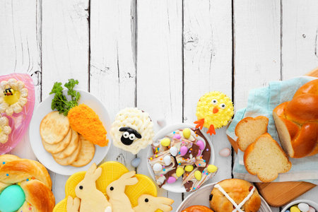 Easter table scene with an assortment of breads, desserts and treats, top view bottom border over a...