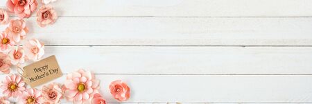 Happy Mothers Day corner border with pink paper flowers and gift tag against a white wood banner backgroundの写真素材