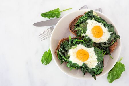 Healthy toasts with spinach and egg on a plate, top view over white marbleの写真素材