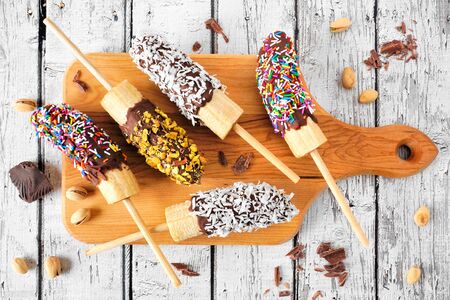 Frozen chocolate dipped banana pops, above view on a wooden platter over white woodの写真素材