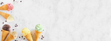 Ice cream cone border with a variety of flavors, top view over a white marble banner backgroundの写真素材