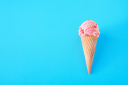 Single cone with pink strawberry ice cream, top view over a blue background