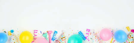Birthday party banner with bottom border on a white background. Top down view with balloons, party hats, streamers and confetti. Copy space.の写真素材