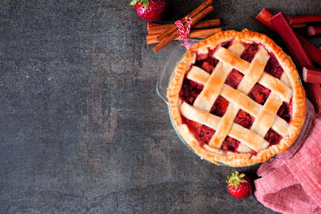 Strawberry rhubarb pie. Overhead view corner border against a dark stone background with copy space. Autumn food concept.の写真素材