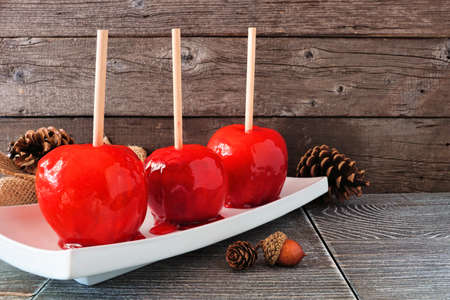 Traditional red candied apples. Side view against a rustic wood background. Halloween or fall treat.の写真素材