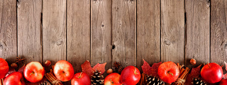 Autumn border of apples, leaves, and fall decor. Top view on a rustic wood background with copy...