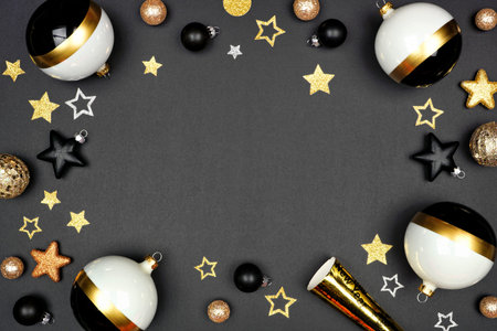 New Years Eve frame of shiny stars, streamers, decorations and noisemakers. Above view on a black...